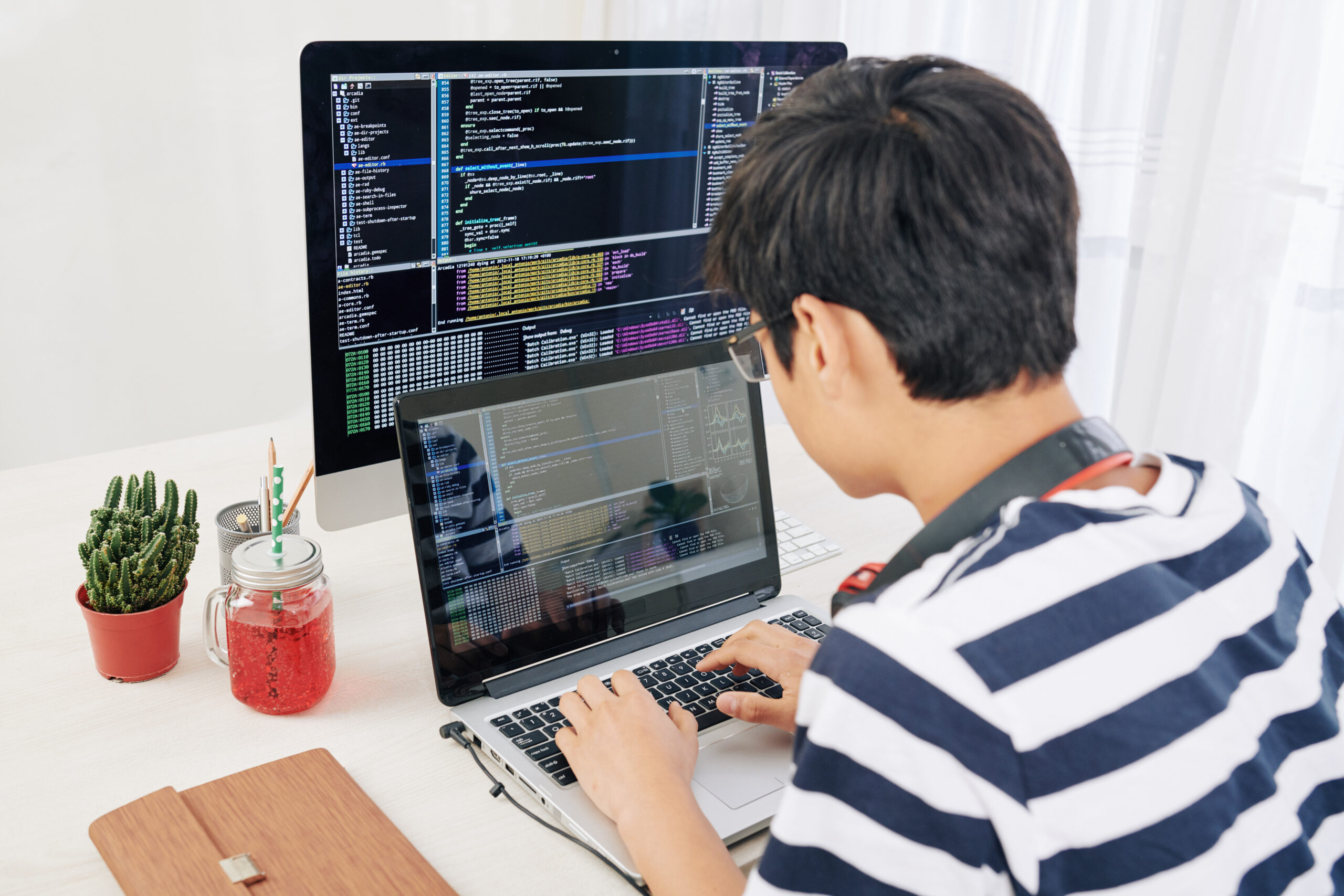 Genious teenager working on laptop, programming code on computer screen in background